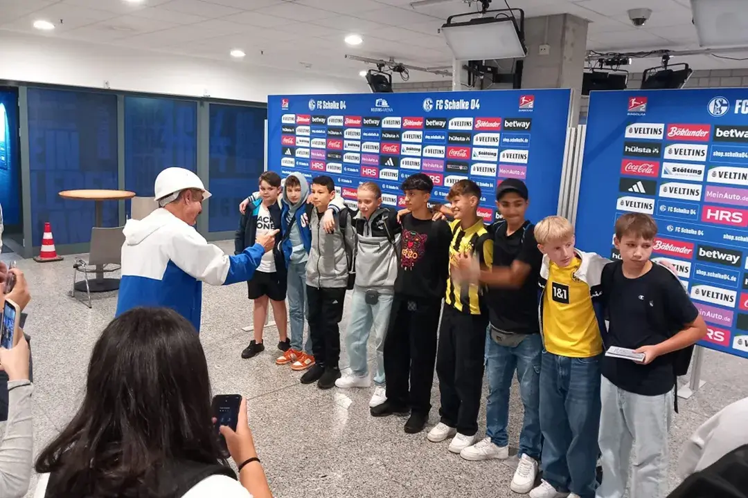 Das Foto zeigt Dinslakener Schüler*innen der Gesamtschule Hiesfeld vor der Sponsorenwand des FC Schalke 04 im Rahmen des Projekts Spurensuche